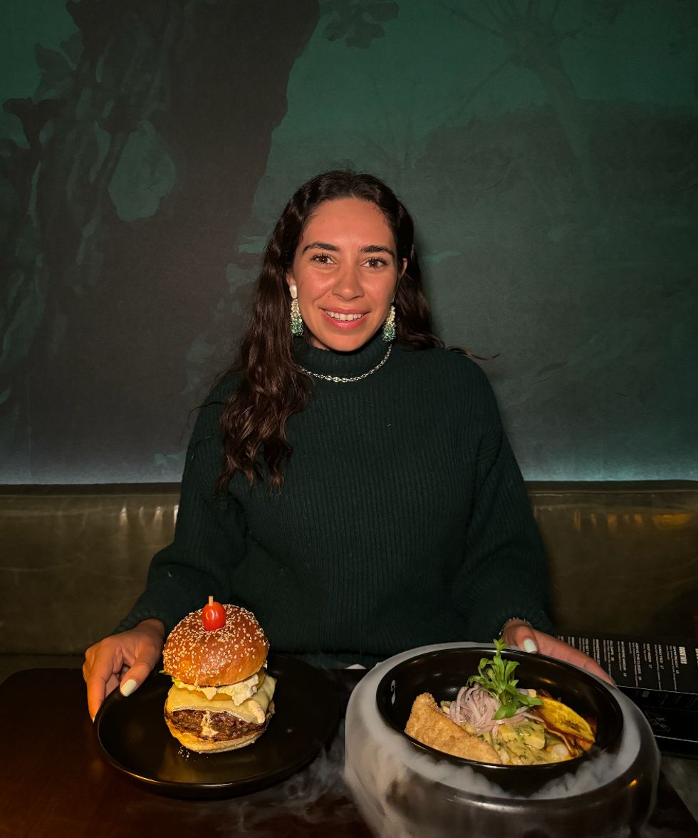 The author sitting at a restaurant with a burger and ceviche in front of her.