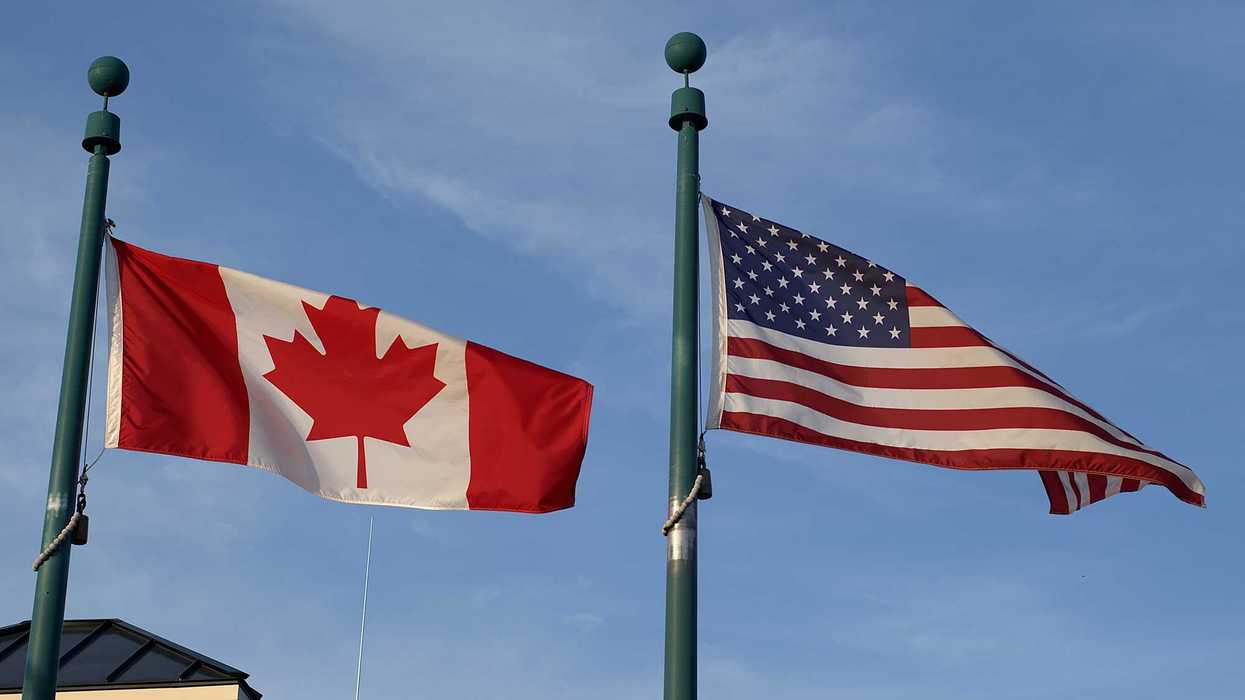 The Canadian and American flags flying side by side on green poles against a blue sky.