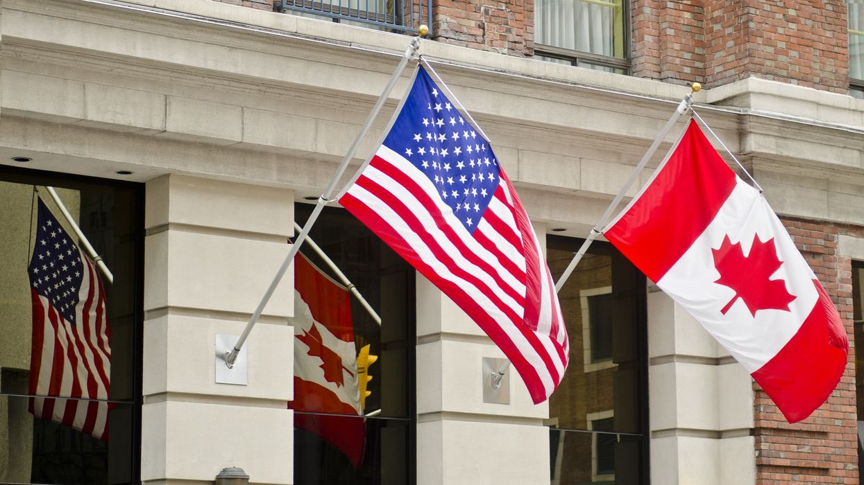 The Canadian and US flags wave side by side on the side of a building in Ottawa, Canada.
