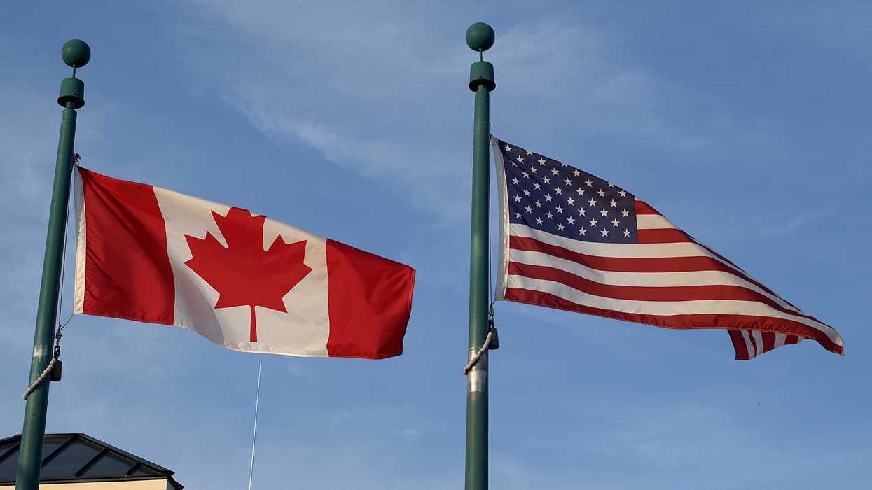 The Canadian flag and the American flag flying side by side on separate flagpoles against a blue sky.