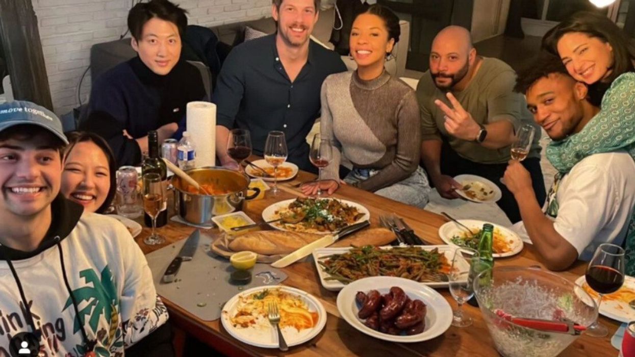 The cast of the show The Recruit smiling for the camera as they sit around a table filled with food.