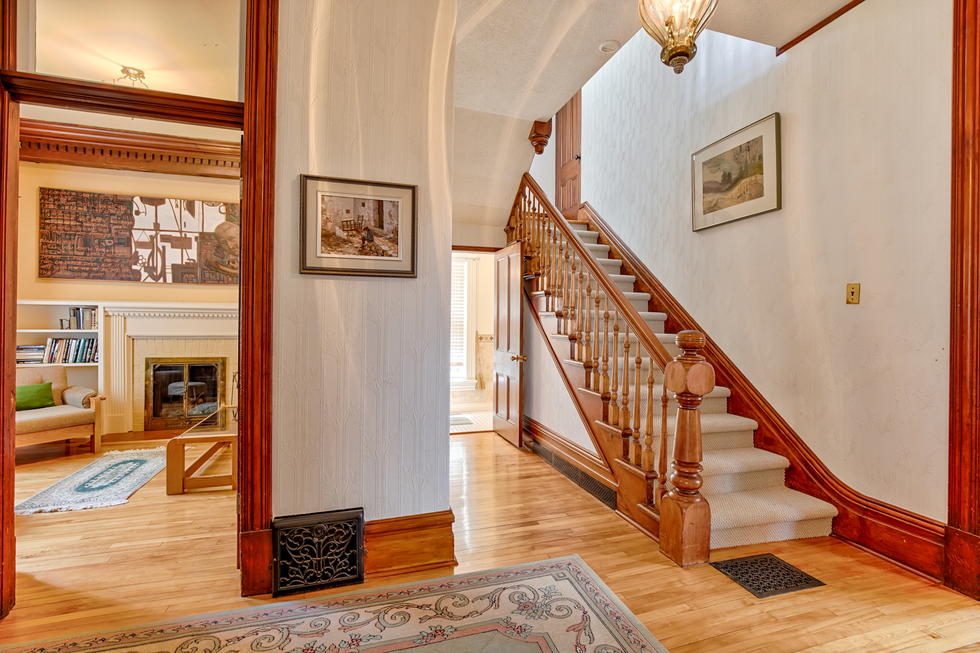 The entrance of the mansion that includes a staircase with steps covered in carpet, hardwood floors and white walls.