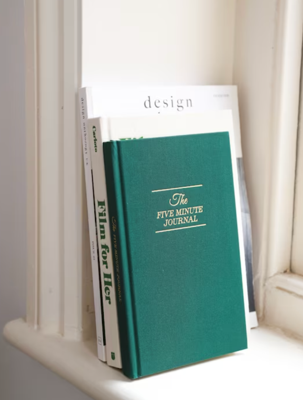 The Five-Minute Journal with other books on a window sill.