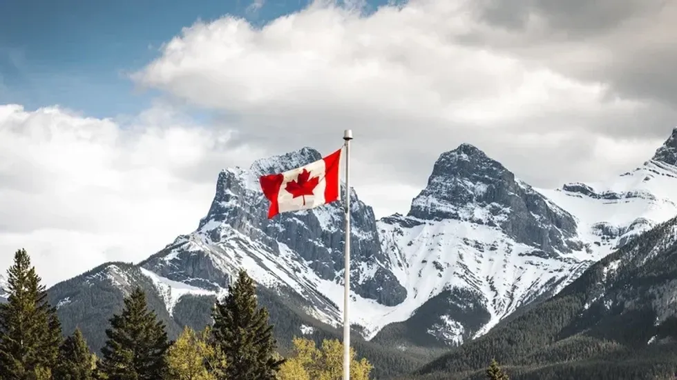 The flag of Canada with snow-covered mountains in the background.