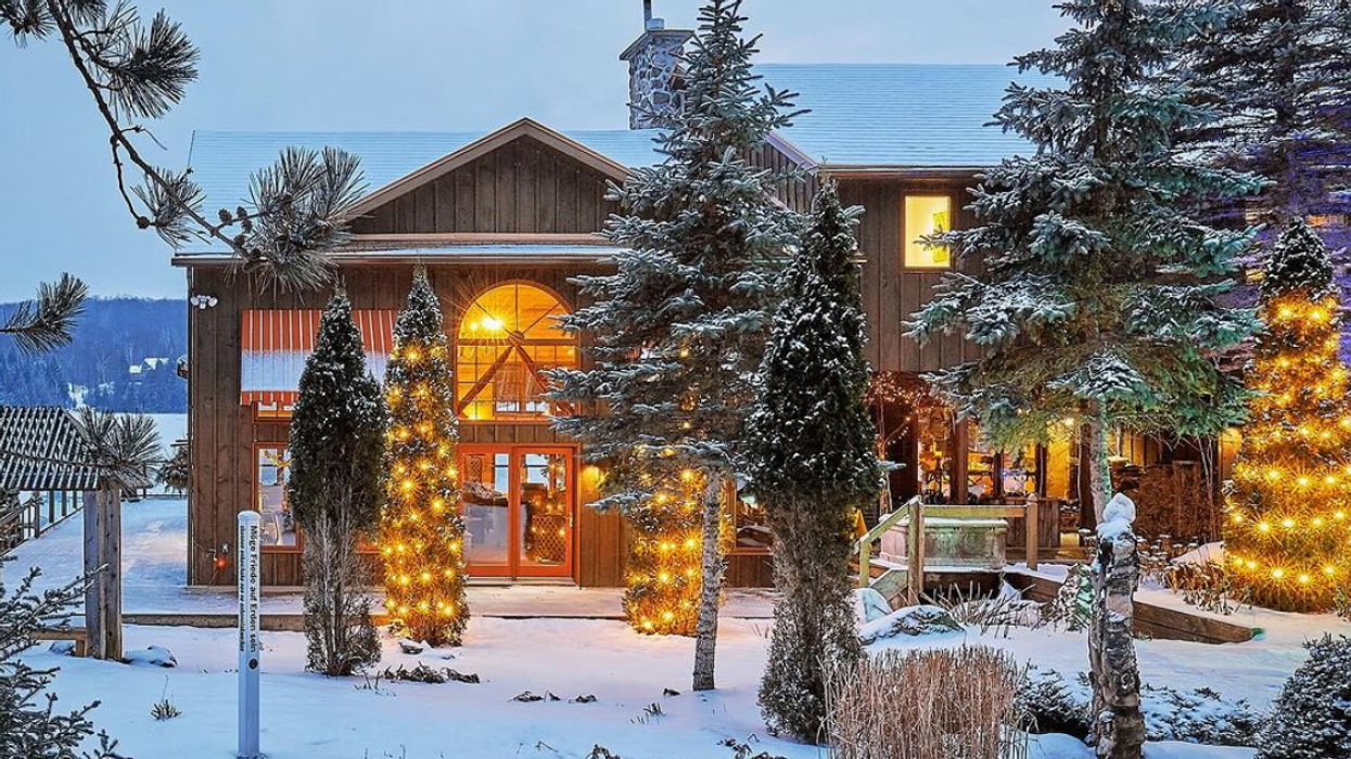 The front of Grail Springs Retreat in the snow lit from the insight and surrounded by trees decorated with lights.
