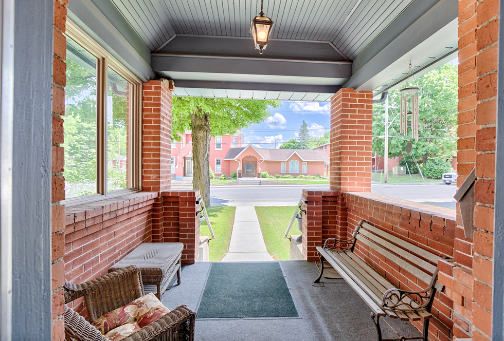 The front porch of the mansion surrounded by red brick walls, and two wooden chairs.