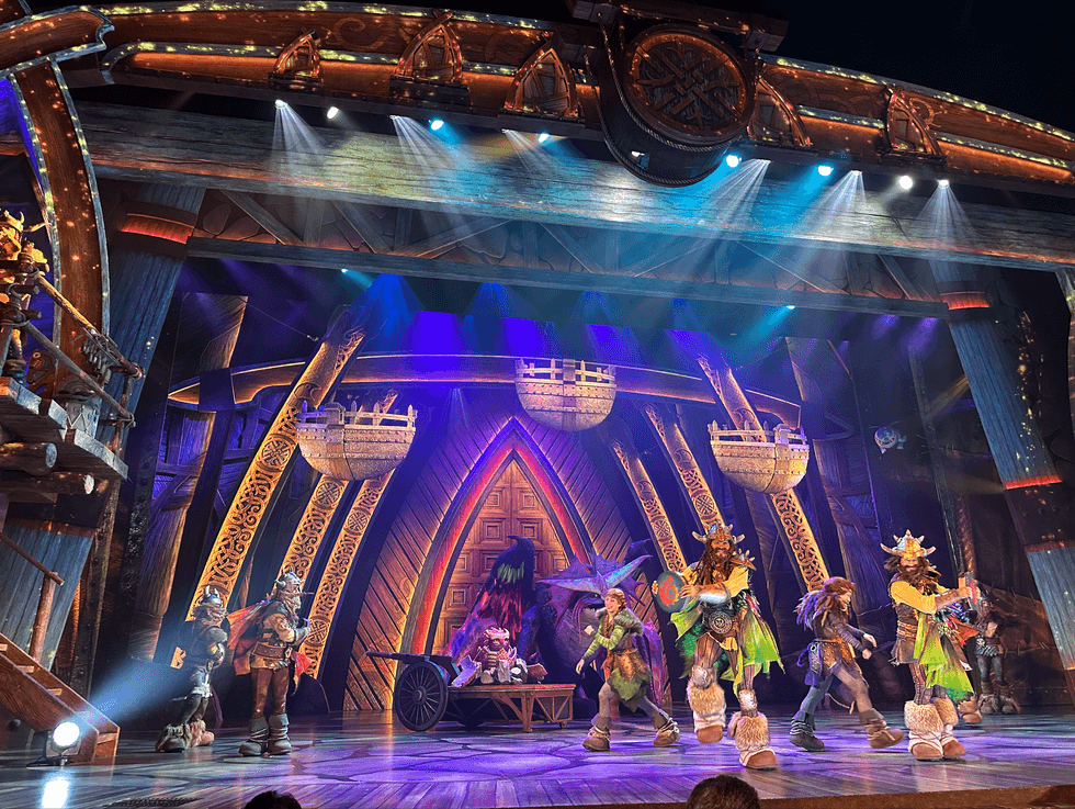The stage of The Untrainable Dragon live show at Epic Universe, featuring Viking performers, dragon puppets, and dramatic purple and blue stage lighting against an ornately carved wooden set.