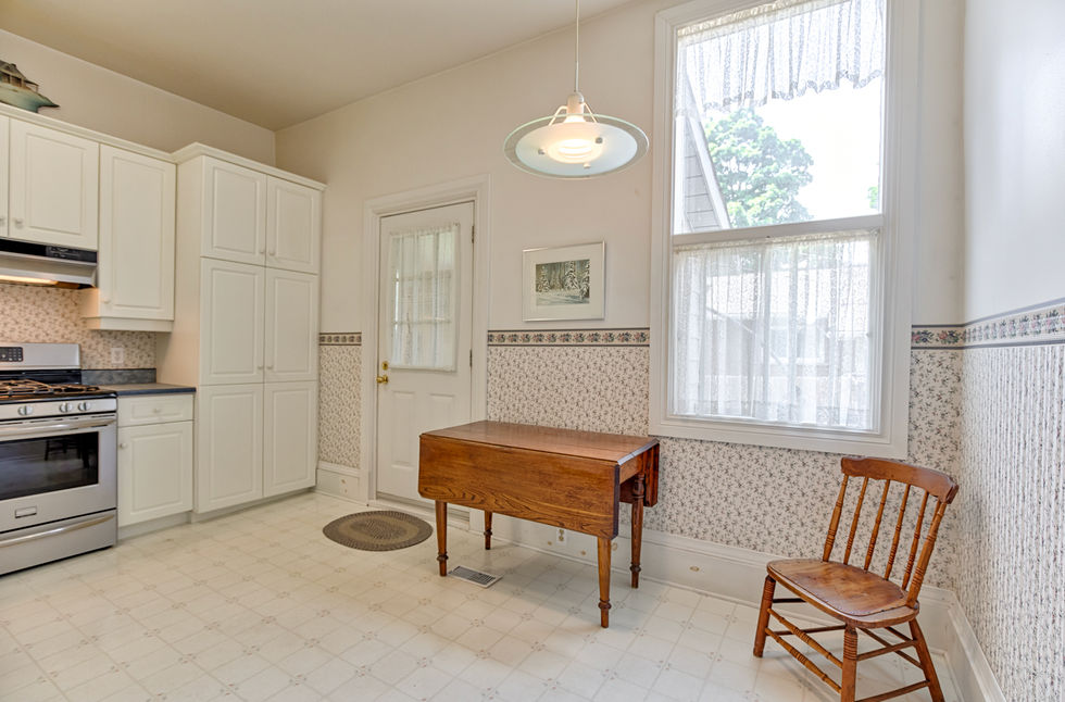 The vintage looking kitchen with floral walls, white cabinets, an oven and a wooden kitchen table.
