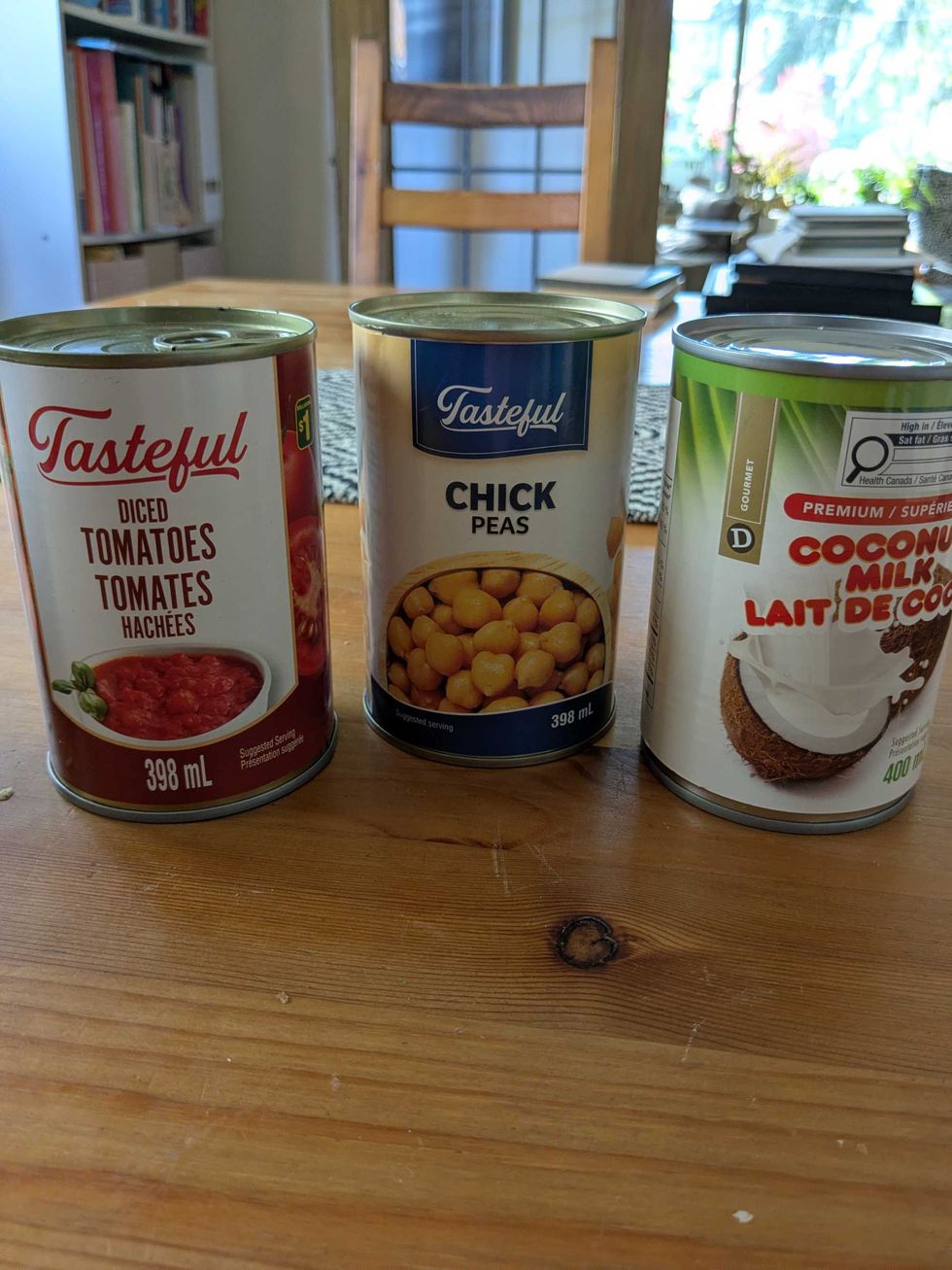 Three cans in a row on a table - one each of tomatoes, chickpeas, and coconut milk