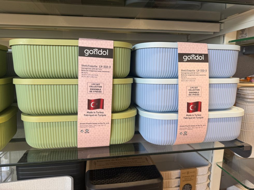 Three green storage boxes stacked next to blue storage boxes on a store shelf.