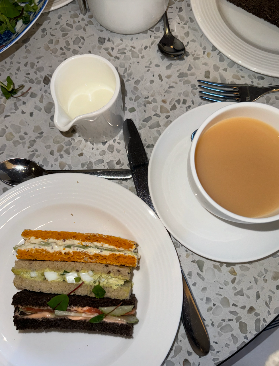 Three of the sandwiches from the afternoon tea on a plate with a cup of tea with milk.