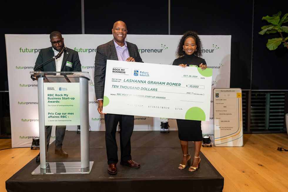 Three people on a dias, two of which hold a giant cheque for $10,000.