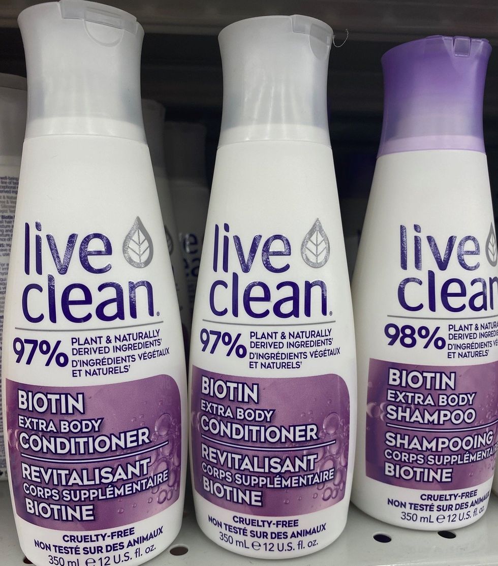 Three white and purple coloured bottles of shampoo and conditioner at a store.