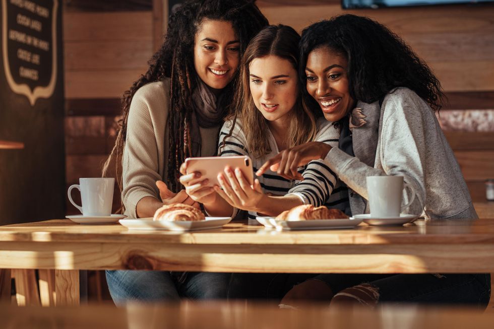 Three women looking at a phone in a cafe.