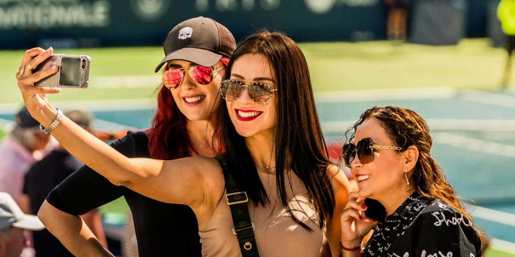 Three women smiling and taking a selfie in the stadium stands during TennisFest Weekend at the National Bank Open in Toronto.