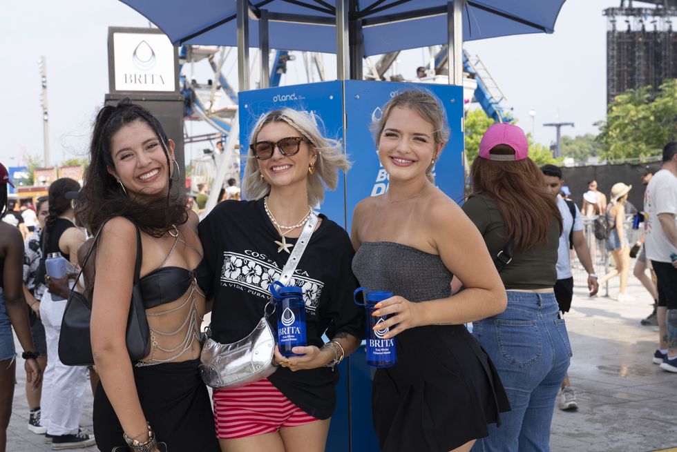 Three young women smiling in front of the Brita water refill station at Osheaga, in Montreal, 2024. 