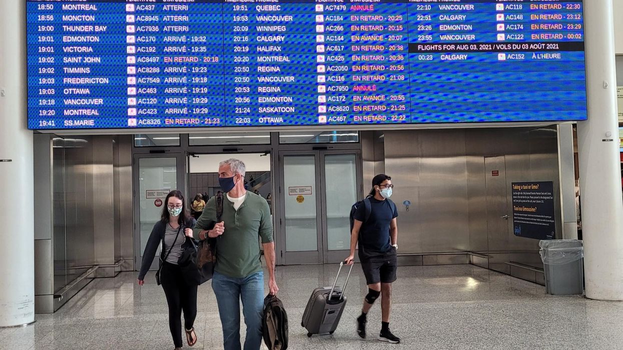 Travellers at Pearson Airport walking in front of a flight board showing delays and cancellations.