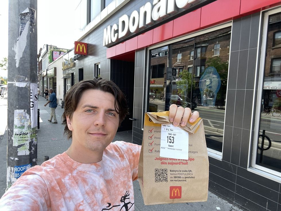 Tristan holding the Big Mac in front of the McDonald's.