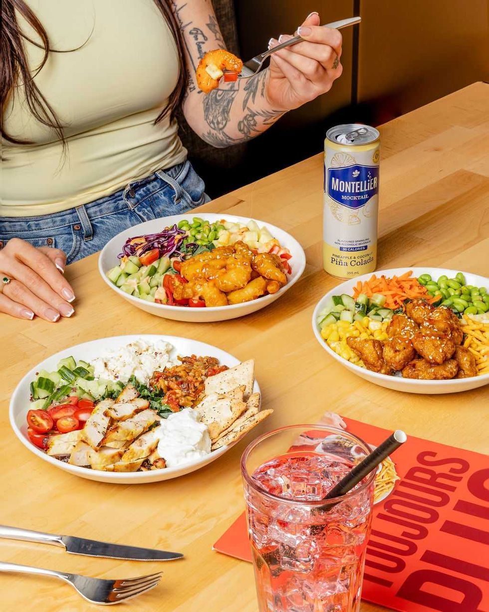 Trois bols-repas color\u00e9s servis avec des boissons sur une table, pendant qu'une personne d\u00e9guste son repas.