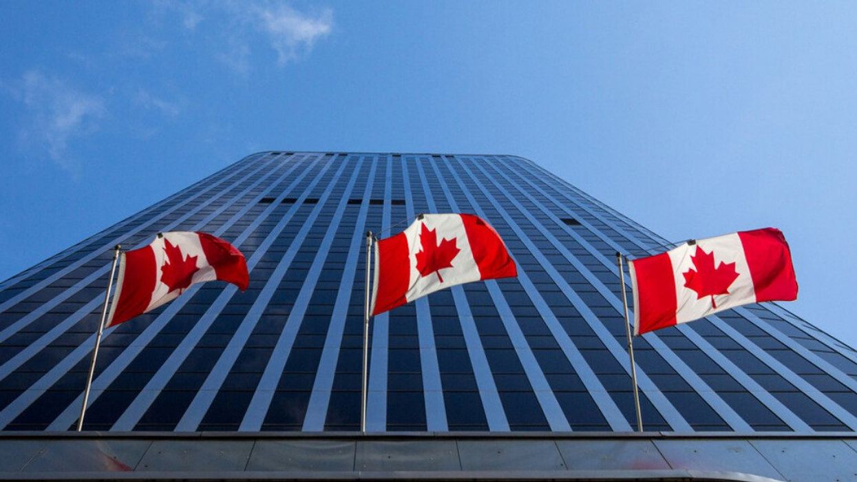 Trois drapeaux du Canada devant un gratte-ciel.