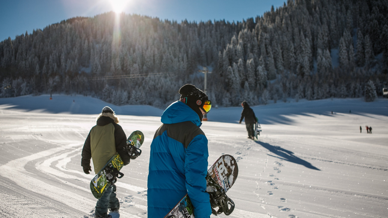 Trois snowboardeurs marchent à travers la neige lors d'une journée ensoleillée d'hiver.