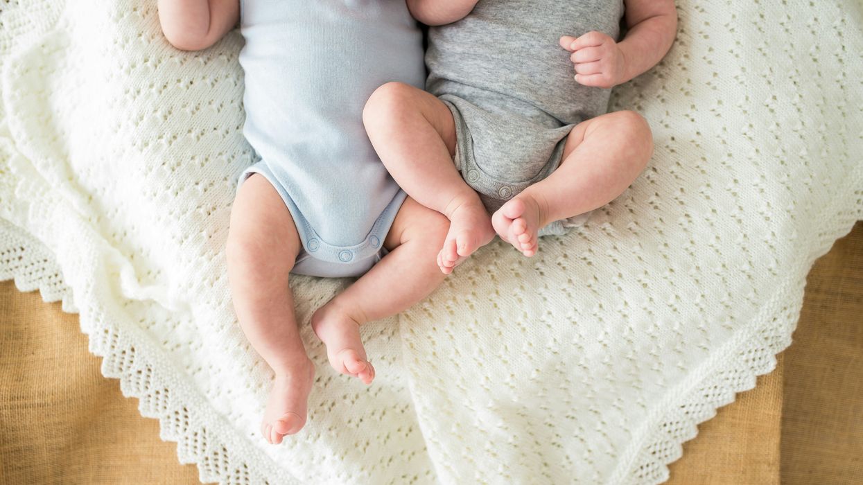 two babies in onesies lying on a blanket