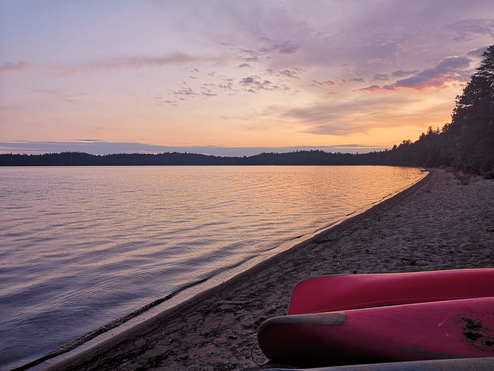 Two canoes on a beach by a lake at sunset.