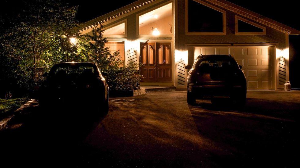 Two cars parked in a driveway of a brightly lit house.