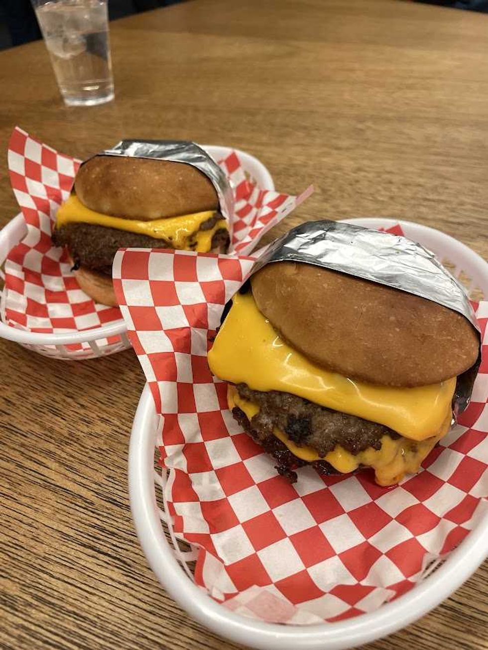 Two cheeseburgers, each wrapped in foil, in a white basket on restaurant table.