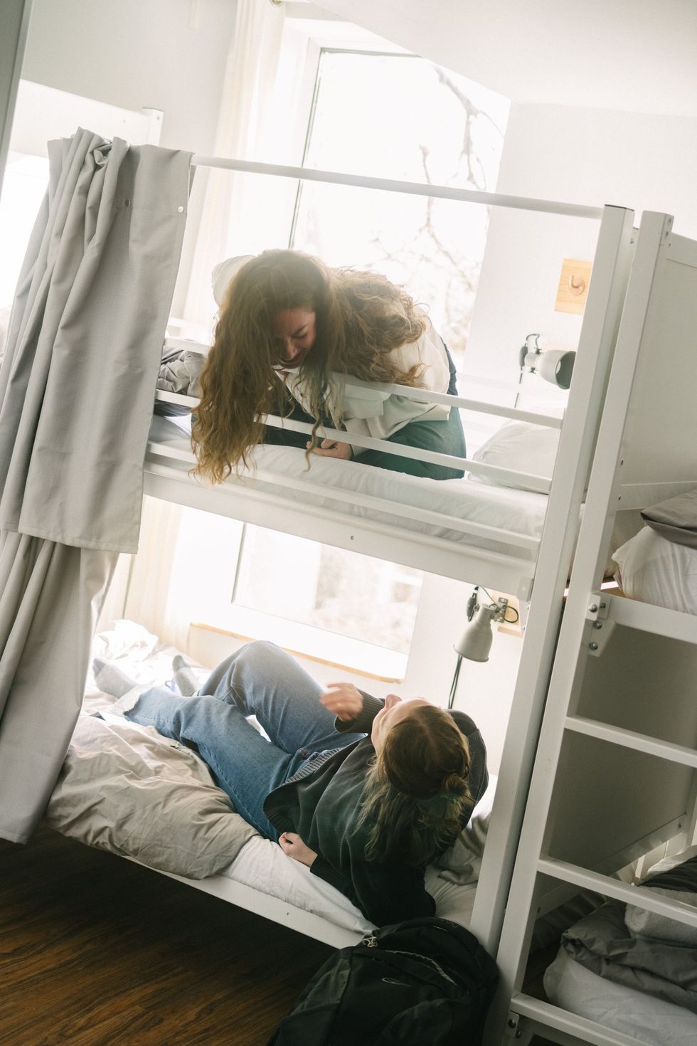 Two friends in a bunk bed having a conversation in a youth hostel dorm room.