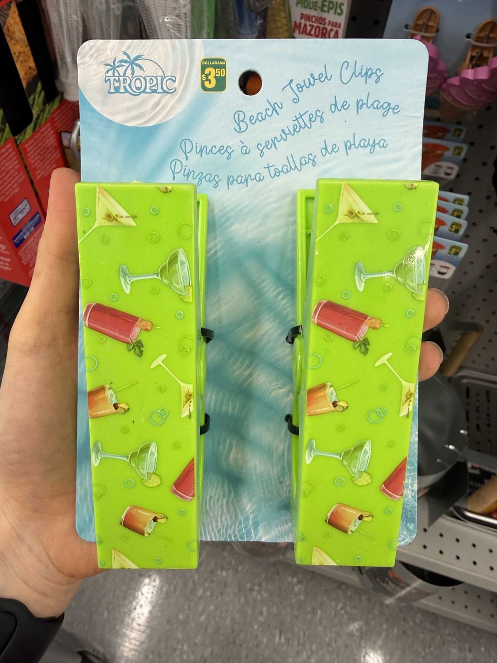 Two green clips with pictures of drinks on them and a label that reads beach towel clips.