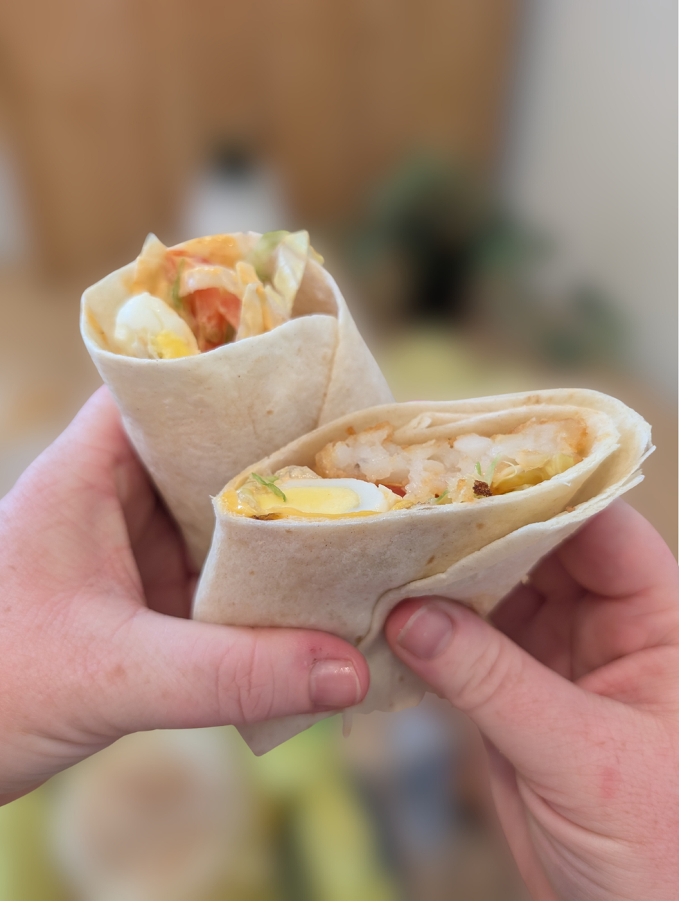 Two hands holding a Spicy Egg & Hash Brown Breakfast Wrap.