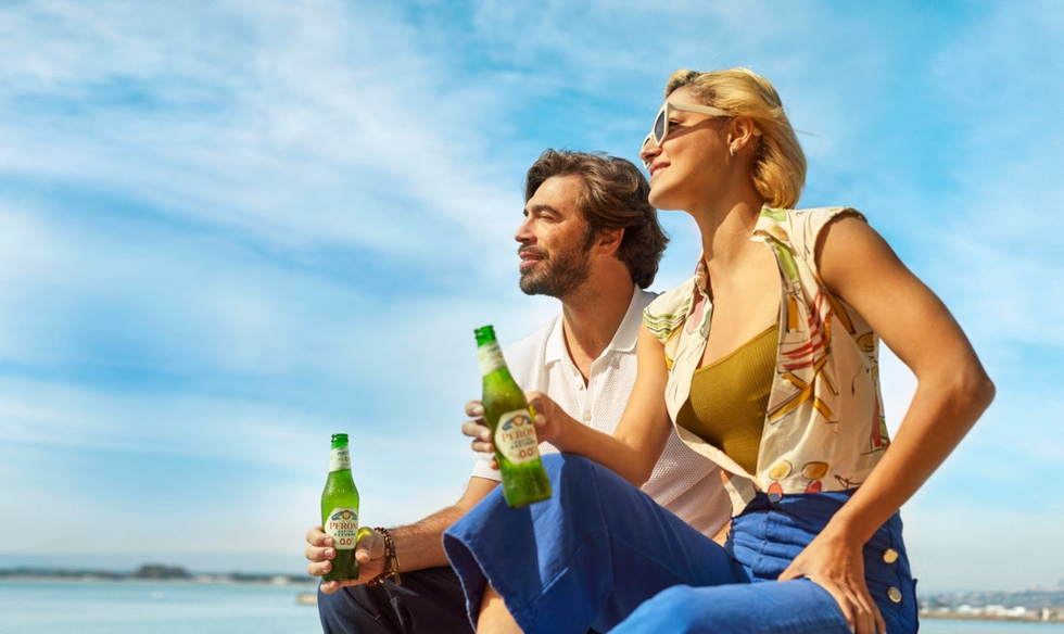 Two people drinking Peroni Nastro Azzurro under a blue sky look out to the horizon.