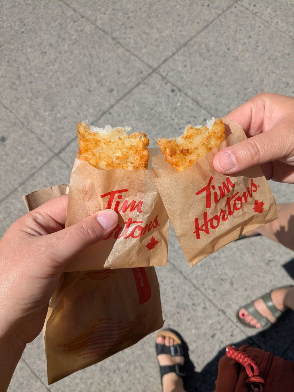 Two people holding and "cheersing" Tim Horton's hashbrowns