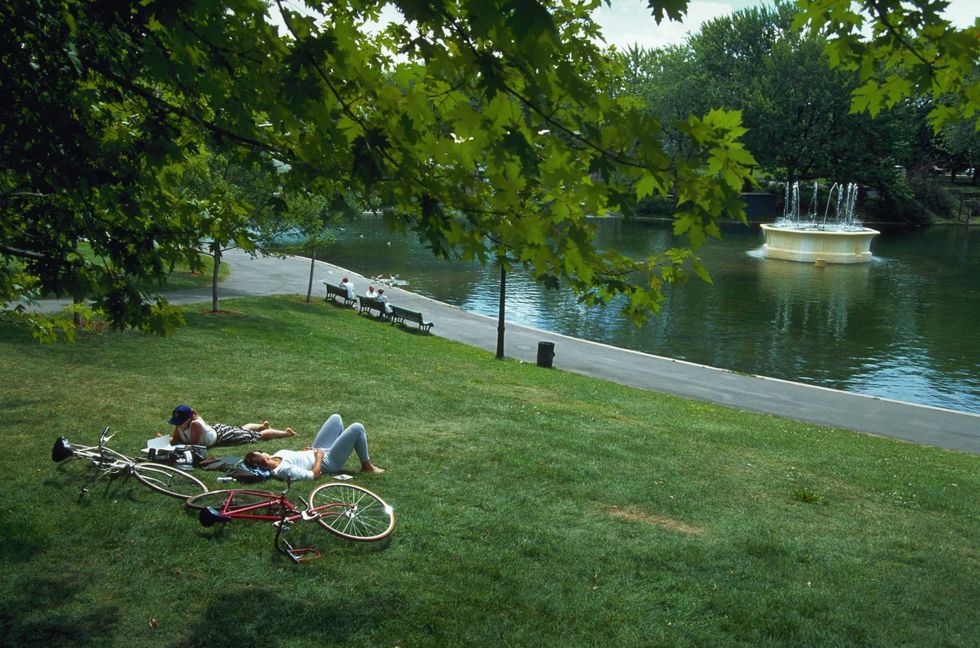 Two people laying on a hill beside bikes along a river.