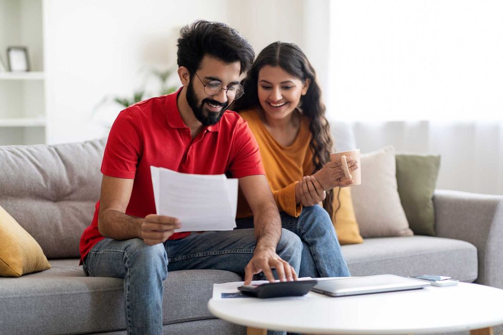 Two people sitting on a couch, looking at a calculator. The person on the right holds paperwork.