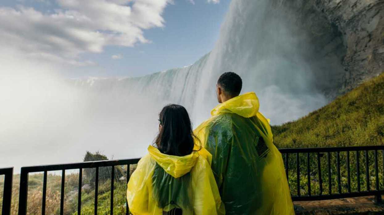 Two people standing beside a waterfall.