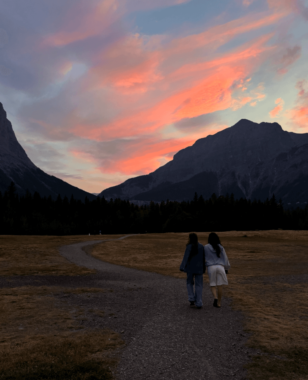 Two people walking on a trail through mountains at sunset.
