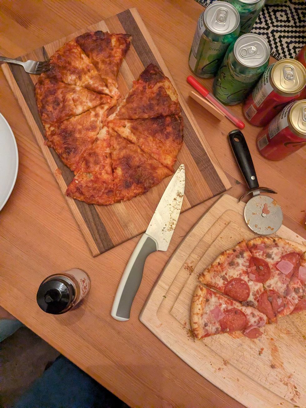 Two pizzas on two cutting boards with a knife and pizza cutter on a table