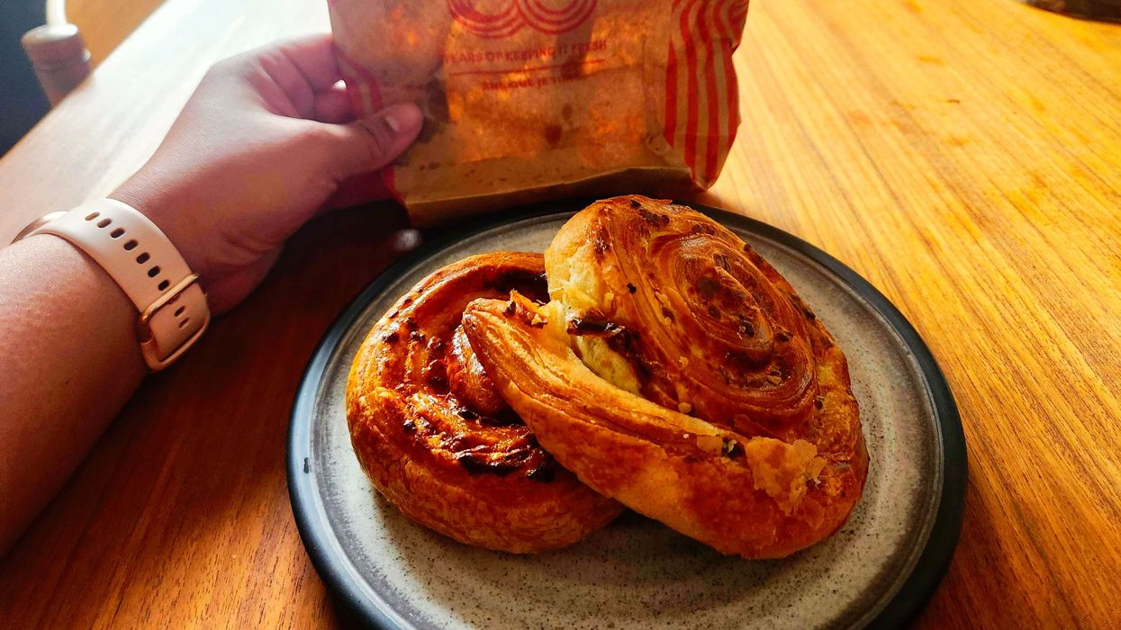 Two Savoury Pinwheel pinwheels on a plate on a wooden table with a hand holding a Tim Hortons bag.
