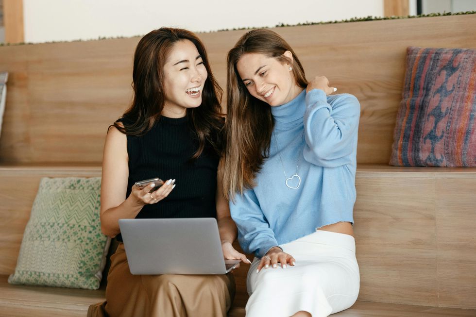 Two smiling women working with laptop and smartphone.