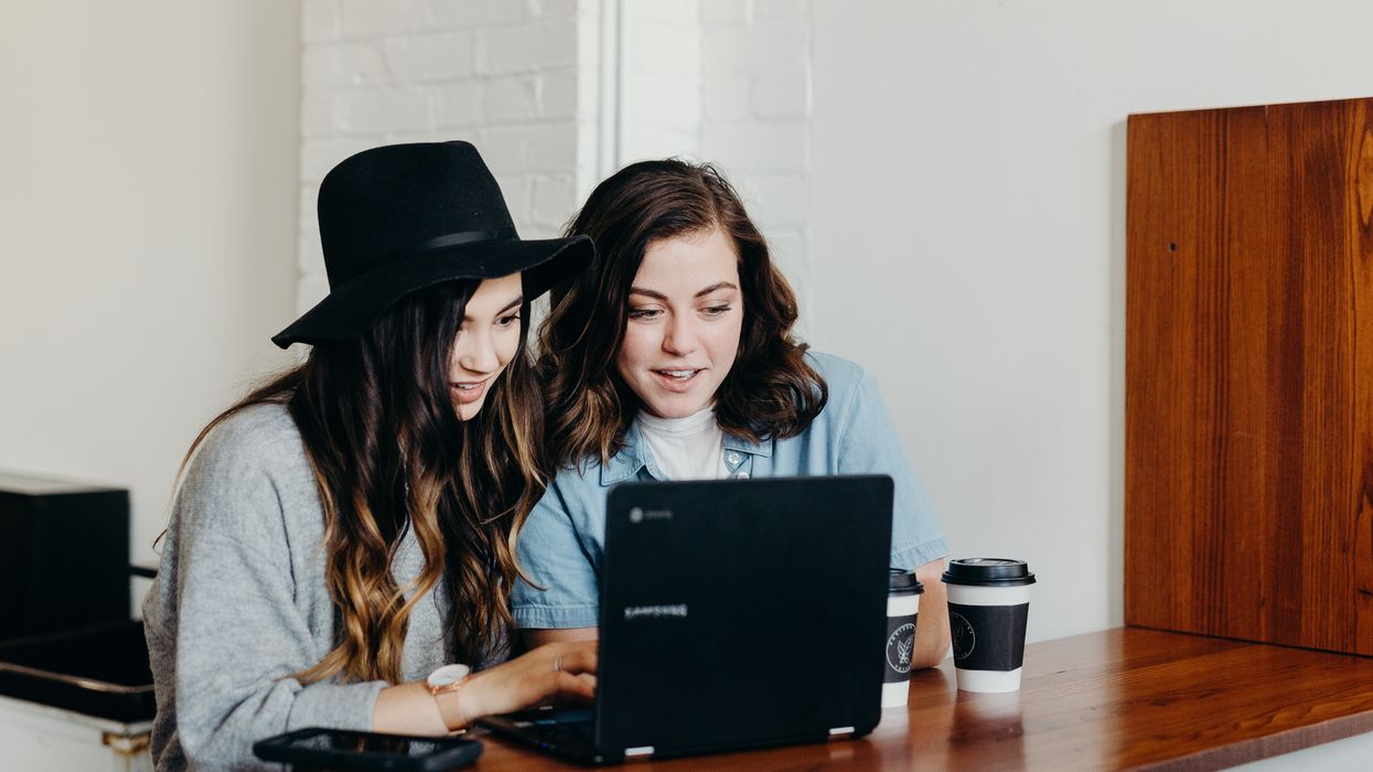 Two women sitting at table looking at laptop together and smiling