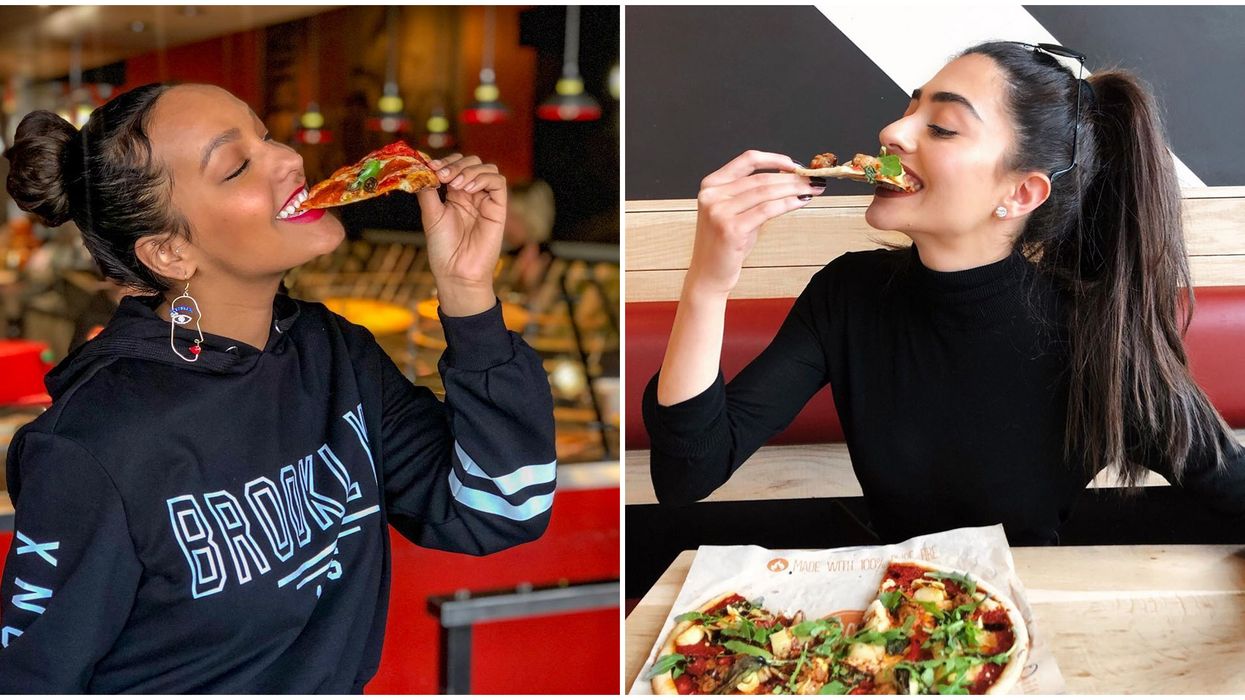 Two women taking a bite of pizza slice while smiling.