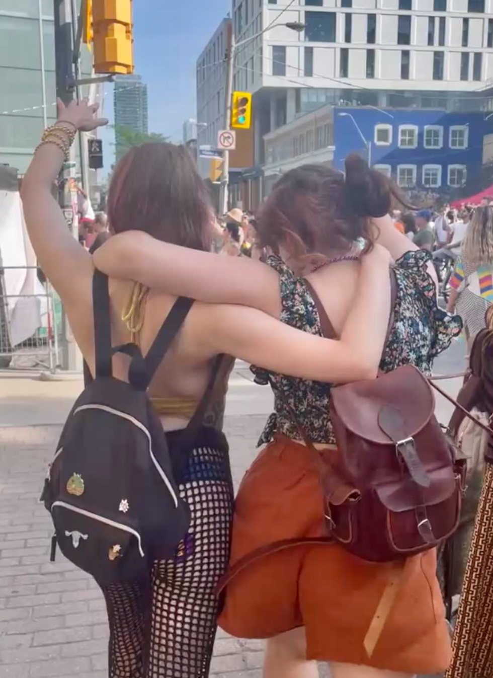 Two women walk arm-in-arm, with their other arms in the air.