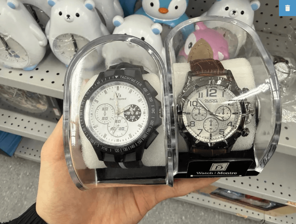 Two wristwatches in display cases held in hand, with bear clocks on shelf behind.