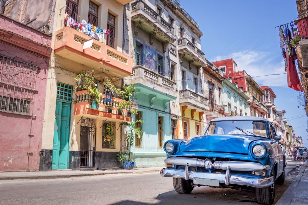 \u200bA blue car is parked on a colourful street in Cuba.