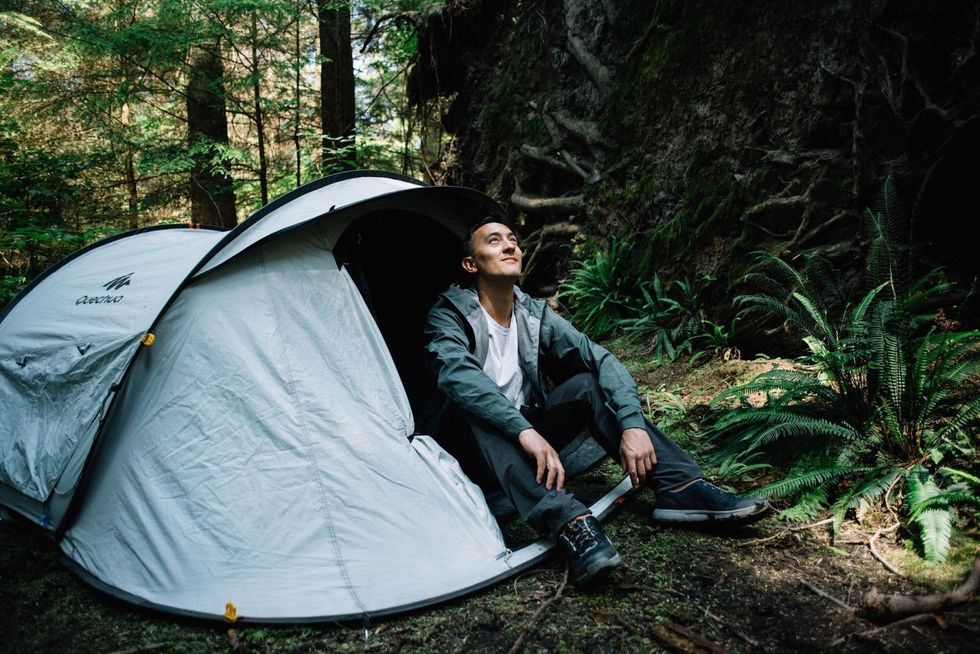 \u200bA person sits in the doorway of a pop-up tent in the woods.