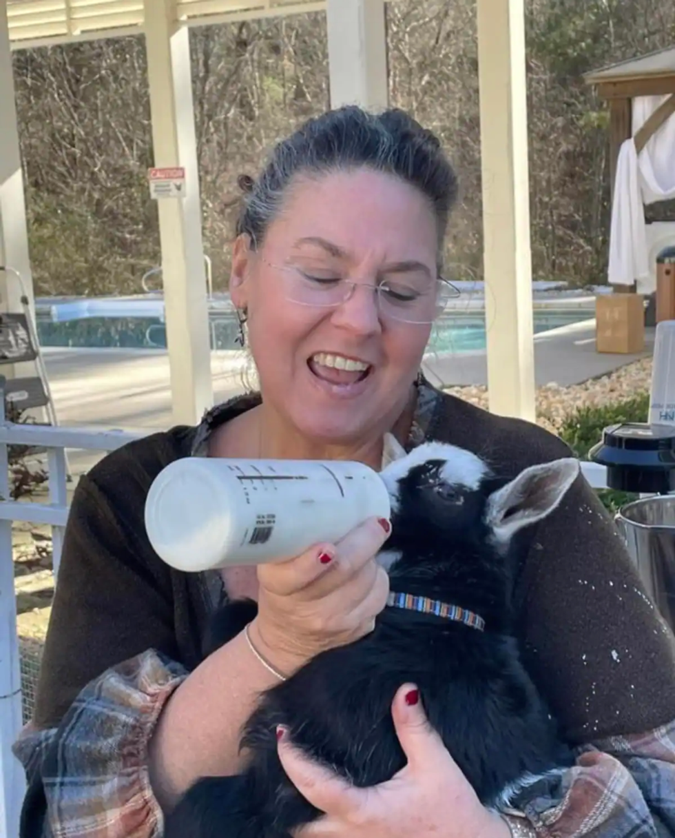 \u200bA woman feeding a baby goat a bottle.