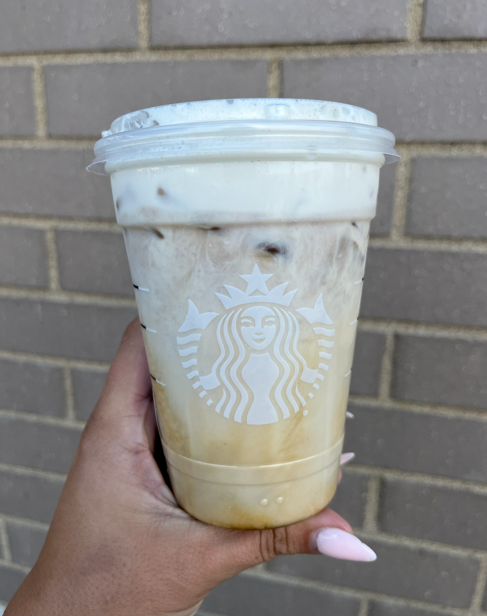 \u200bLe Flat White glac\u00e9 miel, pomme et boisson aux amandes du Starbucks dans une main.
