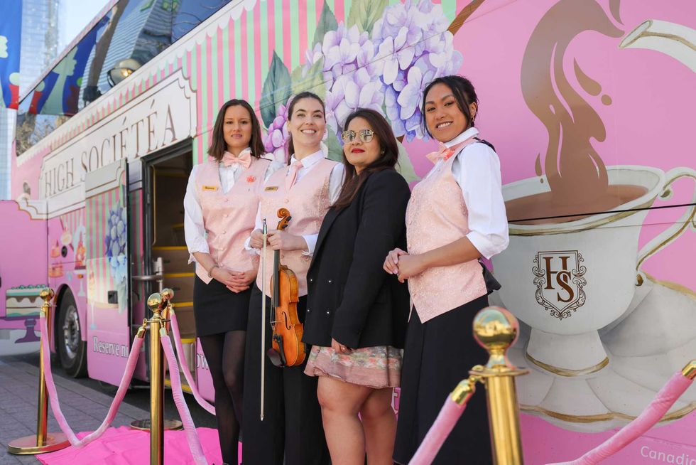 \u200bPeople standing outside a pink bus.